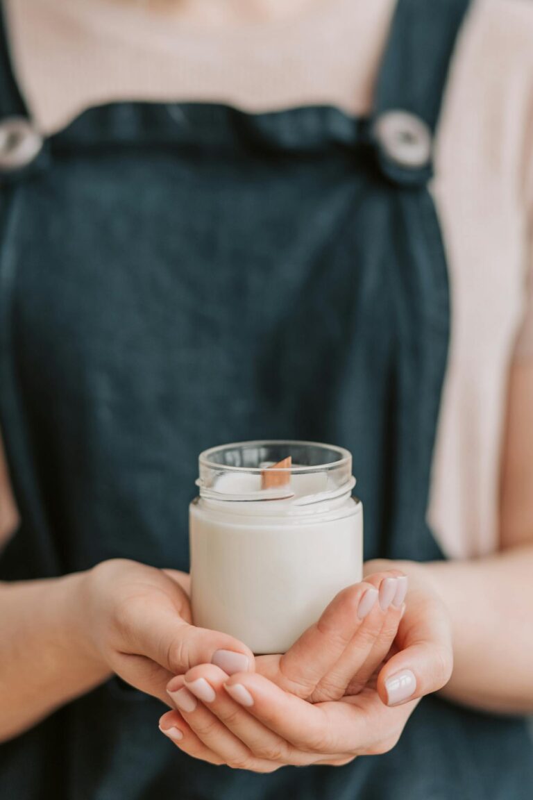 Close-up of a woman holding a handmade candle in a jar with a wooden wick.