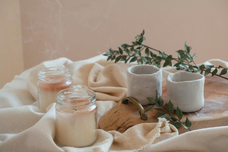 Stylish arrangement of artisanal candles, ceramic cups, and greenery on a rustic tray.